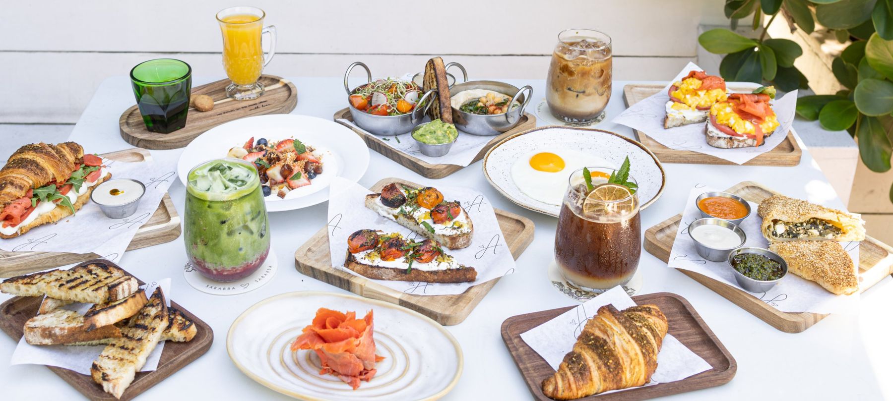 A breakfast spread at Abbalé Café: za'atar croissants, toasts with blistered tomatoes, eggs, yogurt with fruit, iced coffee and matcha